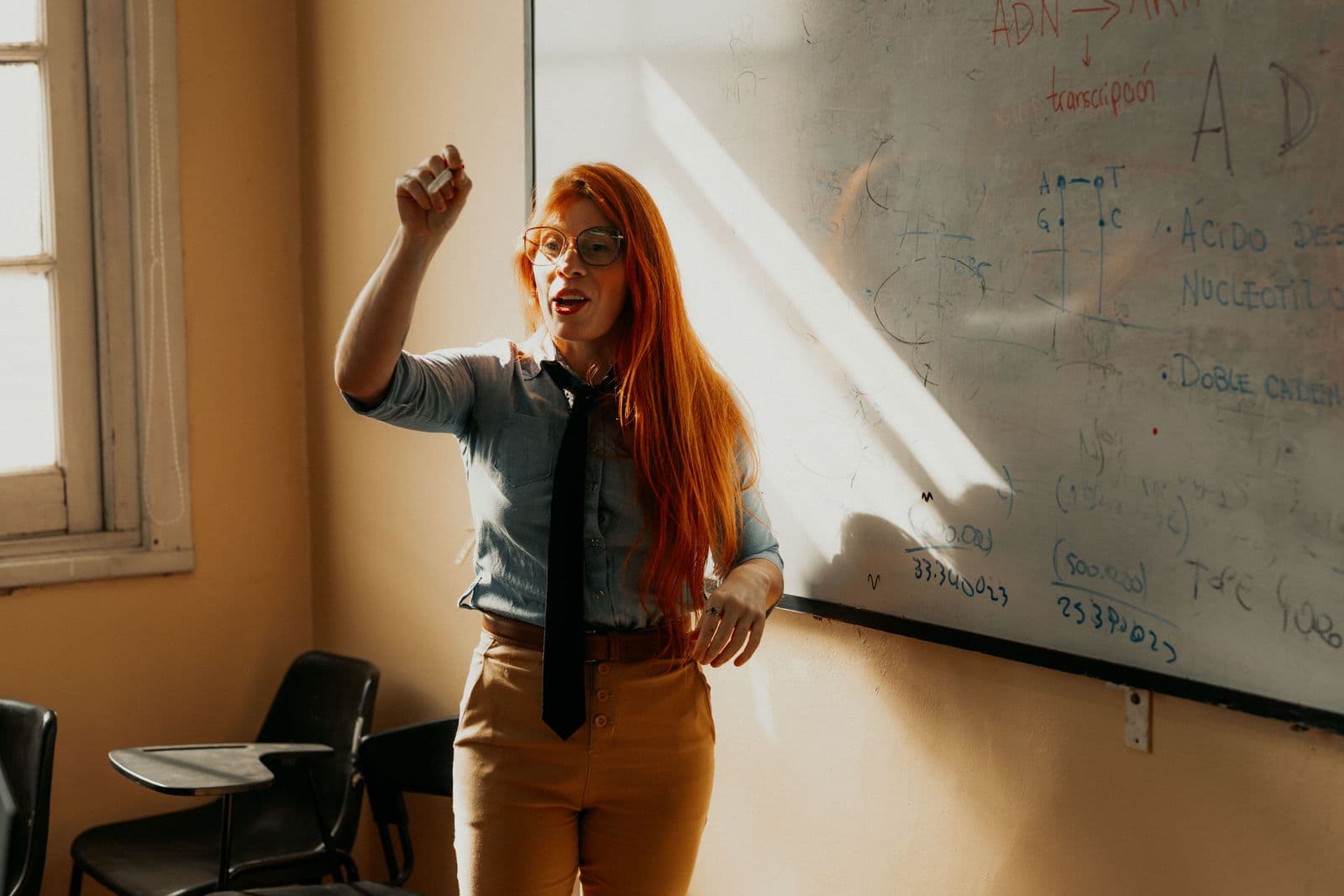 Profesora enseñando frente a una pizarra en una sala de clases latinoamericana